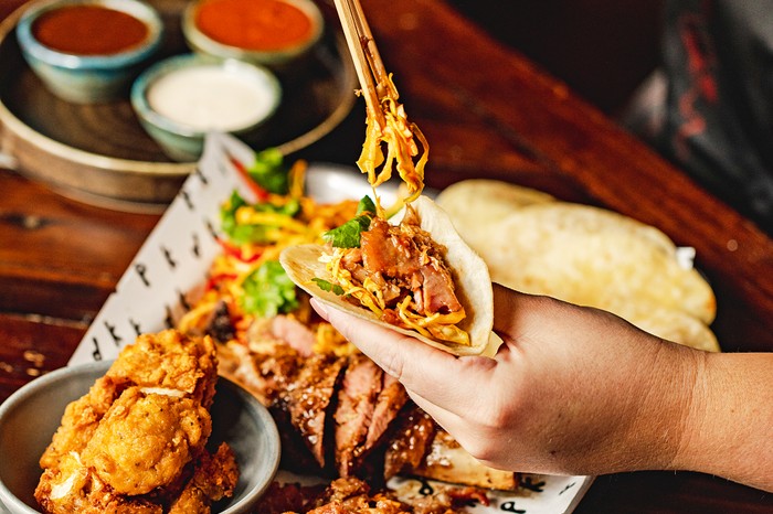 A pair of hands loading up a a taco at Korean Dinner Party