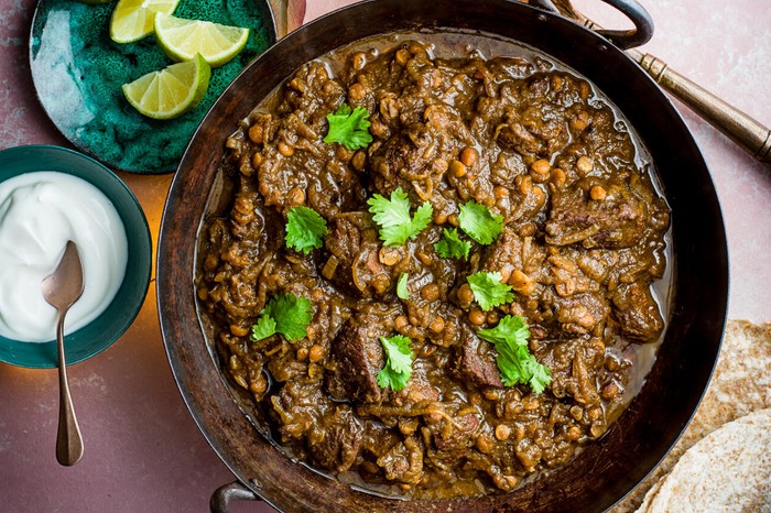 A pan of lamb curry with lime wedges on the side