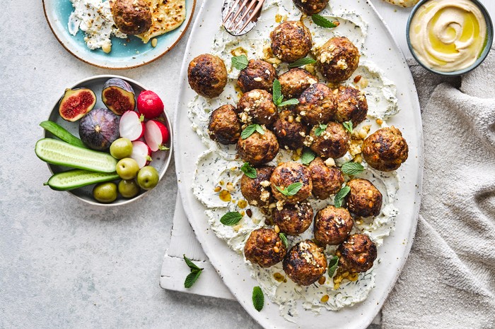 A serving platter full of lamb meatballs with little bowls of crudites and dips surrounding it