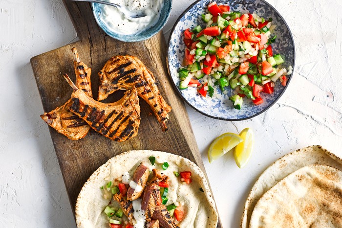 Tandoori Lamb Chops Recipe served on a wooden board with warmed naan bread and a chopped kachumber salad in a blue bowl