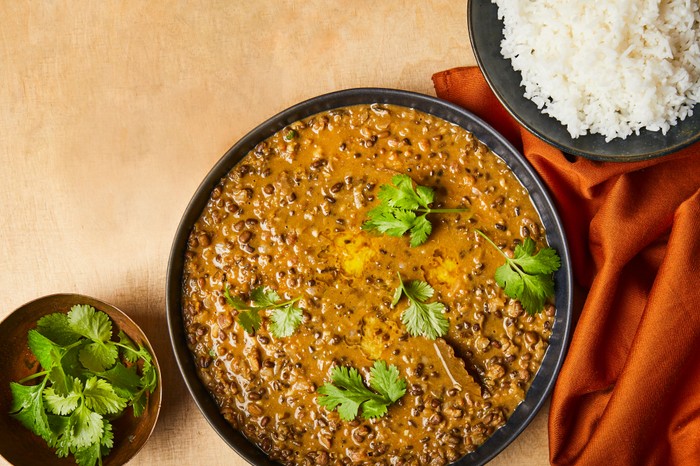 Brown lentil dhal in a bowl with coriander on top next to a bowl of rice