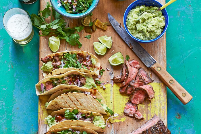 Wooden board topped with beef tacos and side bowls of guacamole and salad