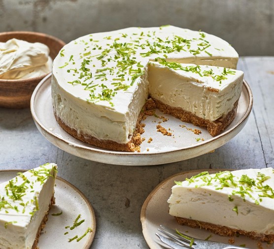 A cheesecake topped with lime zest on a cake stand with a slice taken out