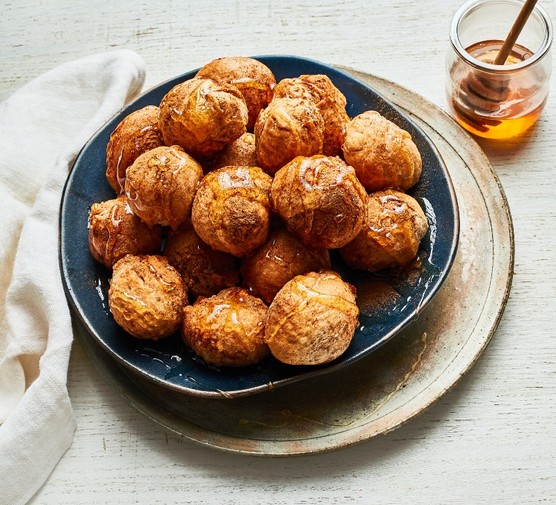 A black bowl of Loukoumades next to a glass pot of honey