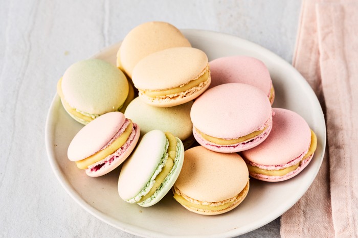 A plate of pastel-coloured macarons on a white surface with a pink linen napkin