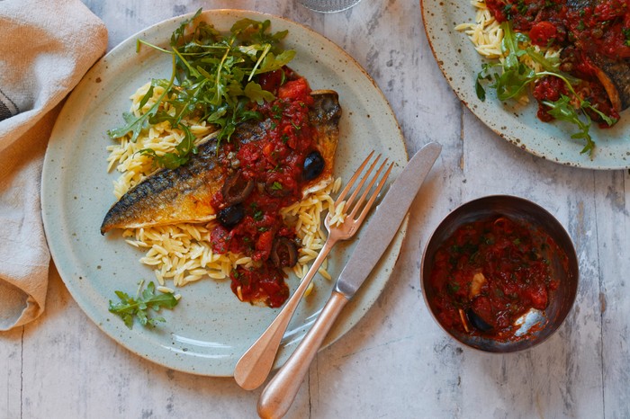 A mackerel fillet on a bed of orzo pasta with a tomato sauce and rocket leaves