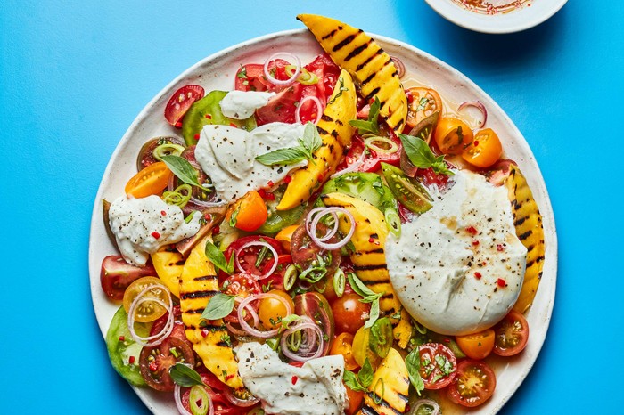 A mango and burrata salad on a white plate against a blue background