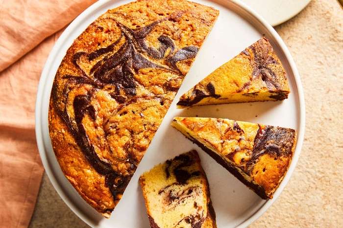 A round marble cake with three slices cut out on a cake stand