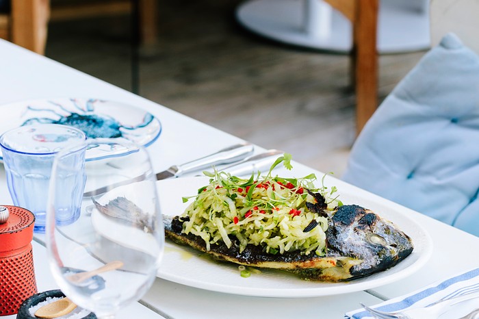 A table with a white plate topped with cooked fish and a green salsa