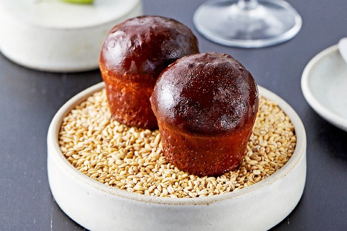 Two dark brown shiny bread rolls on a deep round plate next to a glass of wine