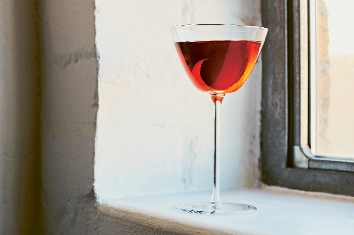 A red cocktail in a stemmed glass on a windowsill