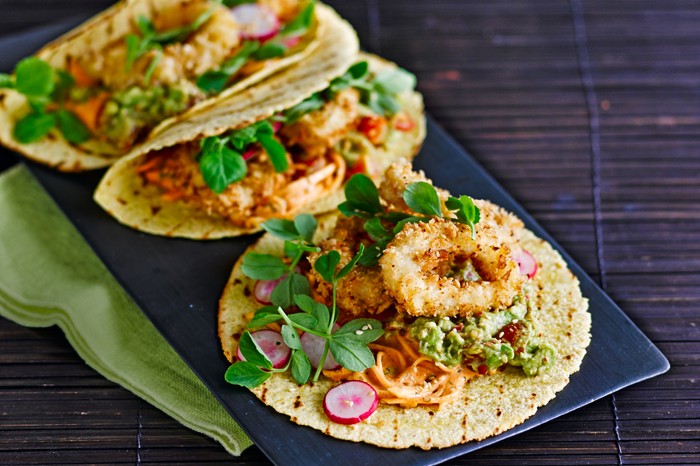 Buttermilk fried squid and kimchi tacos with sliced radishes and pea shoots on a black slate