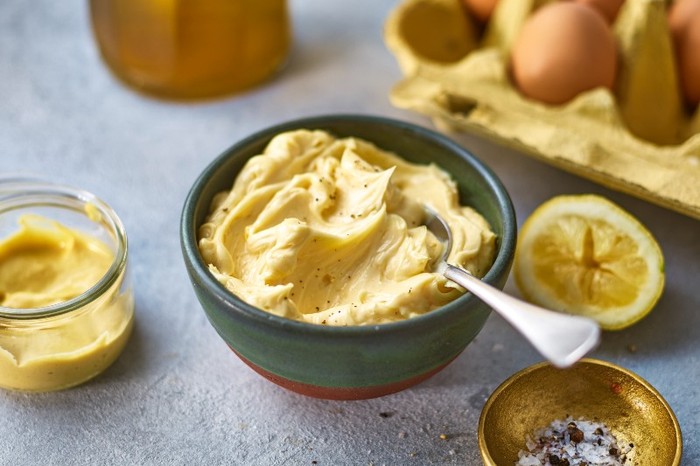 a small grey bowl of yellow mayonnaise next to a carton of eggs