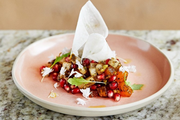 A pastel pink plate topped with pomegranate seeds and mooli on a marble stone table top