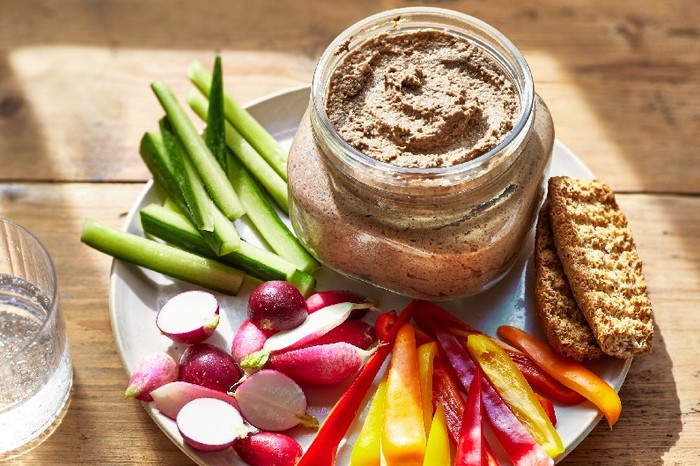 A glass pot of mushroom pate on a plate with crudites