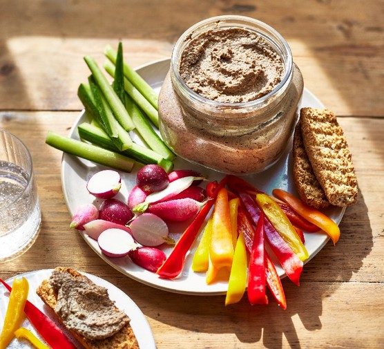 A glass pot of mushroom pate on a plate with crudites