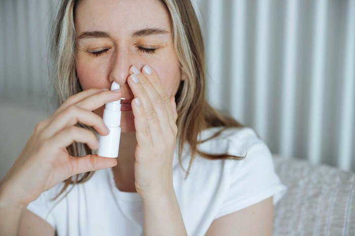Sick young woman using nasal spray Sick young woman using nasal spray