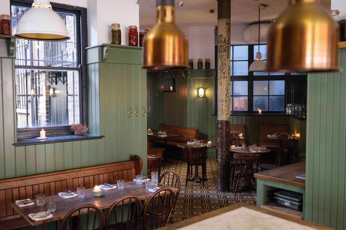 The interiors of Nest restaurant Hackney with olive green walls, wooden tables, copper lights and candles