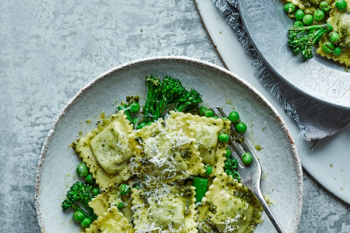 A blue bowl filled with ravioli and green vegetables