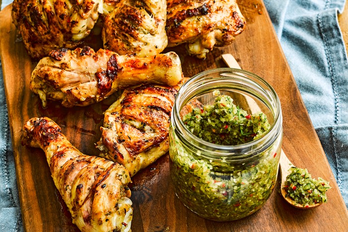 A serving board of chicken legs with a pot of spice rub next to them