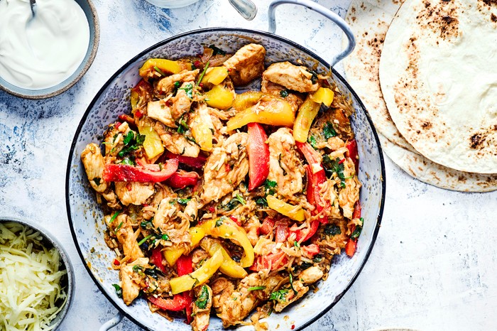 Chicken Fajitas served in a blue enamel dish with onions and peppers. Wraps, cheese, soured cream and guacamole surrounding the main dish