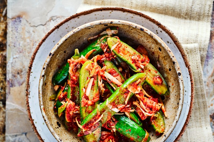 Cucumber Kimchi Recipe Cucumber Kimchi sliced in half with kimchi sprinkled on top, served in a deep speckled blue and grey bowl