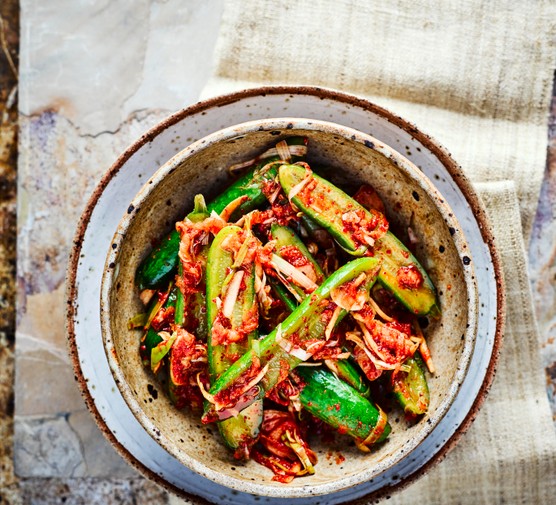 Cucumber Kimchi sliced in half with kimchi sprinkled on top, served in a deep speckled blue and grey bowl