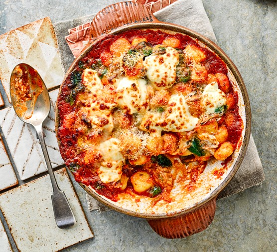 Tomato, spinach and mascarpone gnocchi in a circular dish, next to a serving spoon