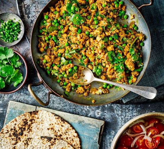 Kheema Matar curry with turkey in a large pot with serving spoon, next to a bowl of coriander