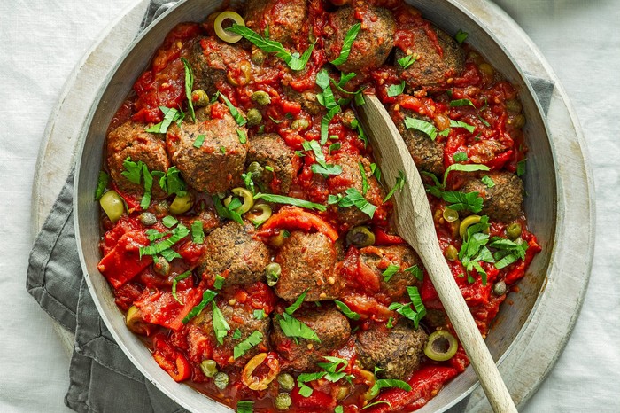 Veggie meatballs in a large pot with a wooden spoon placed inside it