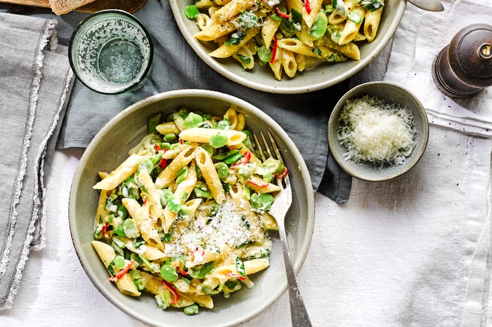 A bowl of pasta with broad beans and sliced chilli on a white linen tablecloth