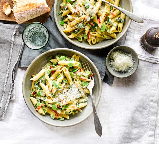 A bowl of pasta with broad beans and sliced chilli on a white linen tablecloth