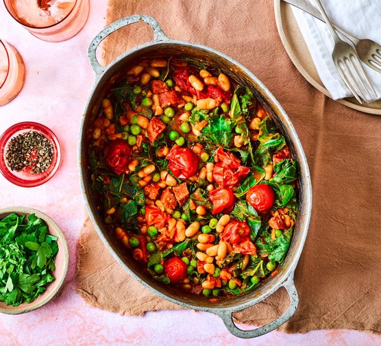 Chorizo, greens and bean stew in a large dish, placed on a table with a side of chopped parsley