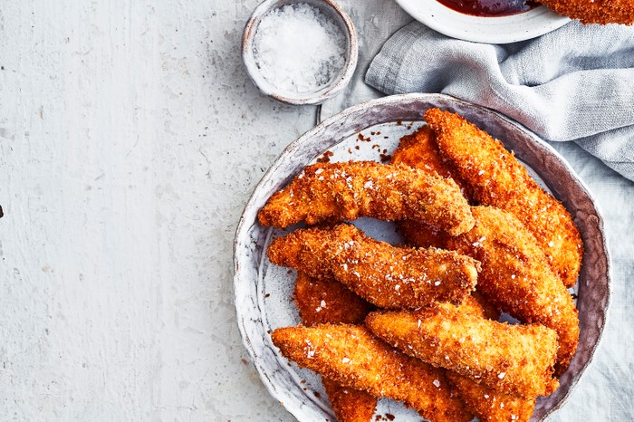 A grey bowl filled with fried chicken strips with a red barbecue sauce on the side