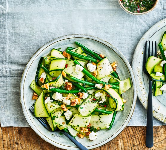 A green courgette salad on a grey plate and light blue background