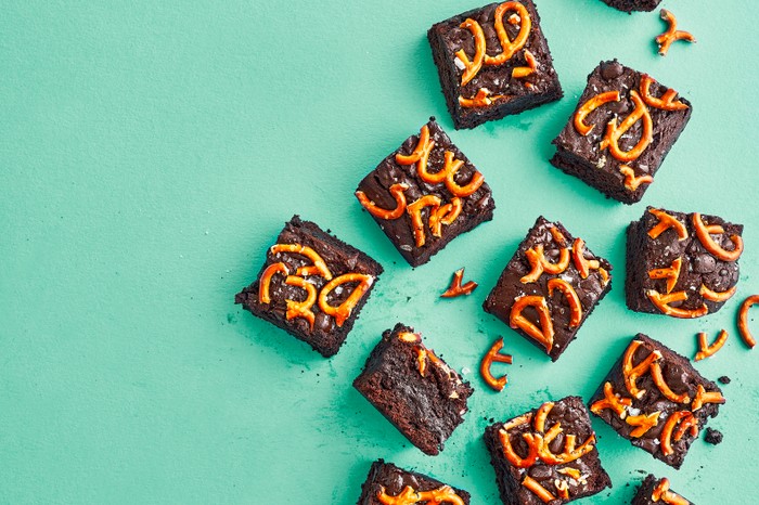 Squares of chocolate brownies topped with pretzels, sat on a teal blue background