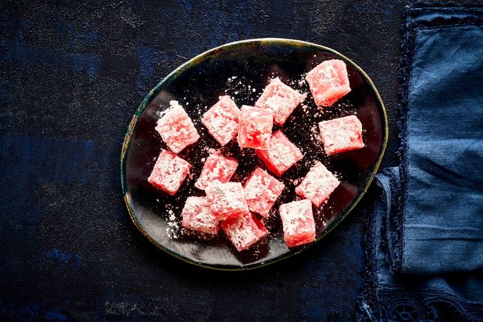 A black plate topped with cubes of pink Turkish delight dusted with icing sugar