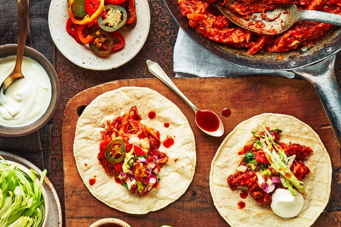 A board topped with two corn tortillas, topped with pulled chicken and limes on the side