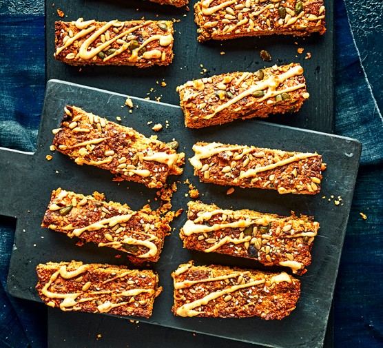 A slate board topped with slices of golden oat flapjacks, drizzled with peanut butter