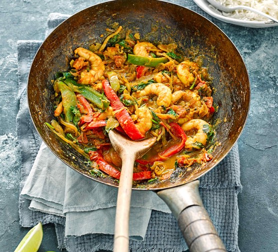 A silver wok is filled with prawns, chopped peppers and green vegetables