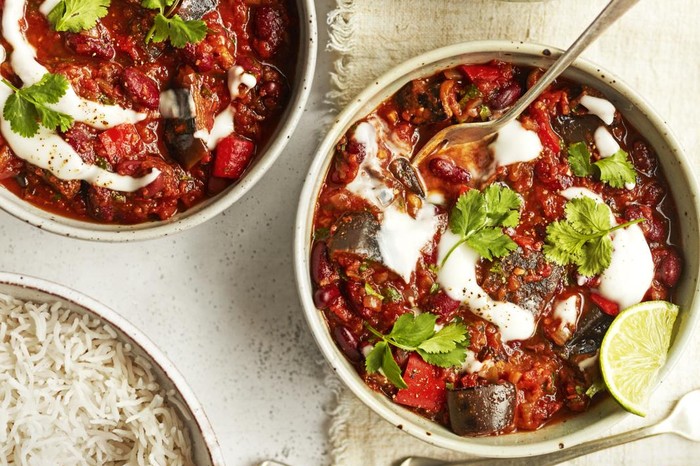 two bowls of veggie chilli with sour cream and lime, and a side of rice