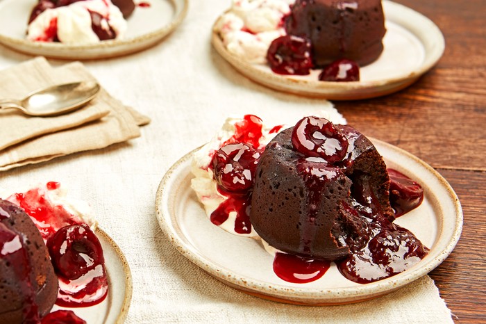 A wooden table topped with plates of chocolate fondant with a dark red cherry syrup