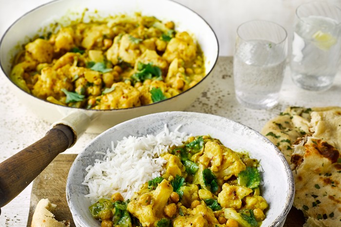 Pan and bowl of chickpea and cauliflower curry next to some naans