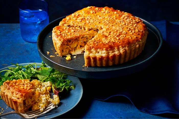 Macaroni and sweetcorn pie on a cake stand with a slice on a plate next to it