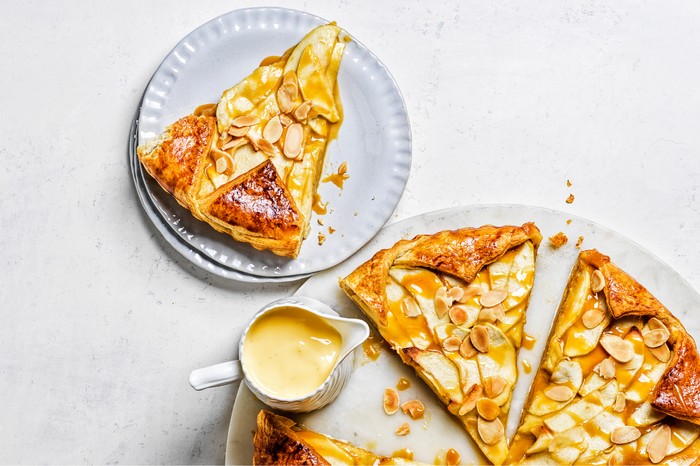 Toffee apple croissant tart with a piece taken out an a jug of custard on the side