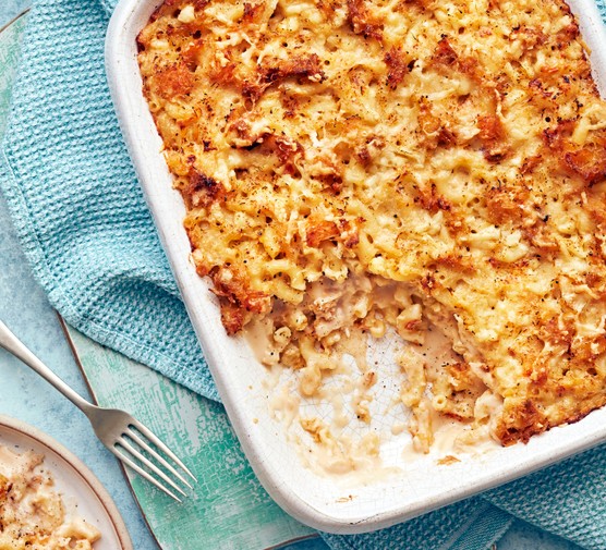 A white oven dish willed with golden mac and cheese on a blue cloth with a silver fork