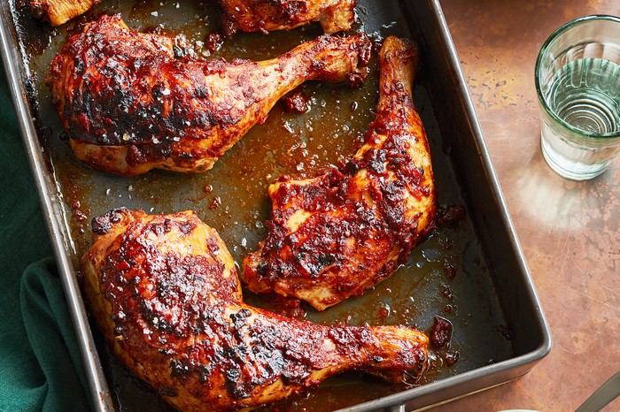 A baking tray topped with chicken legs coated in a brown sauce