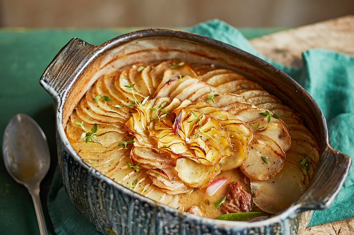 A speckled baking dish filled with a stew and layered with thin and crispy slices of turnip on top