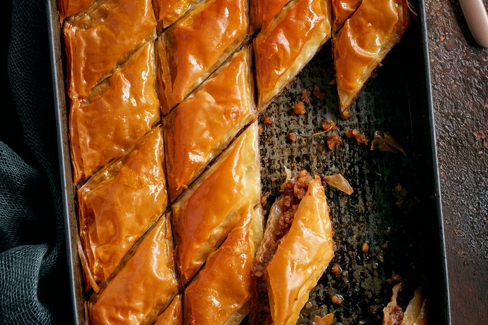 A black baking tray filled with crispy filo pastry triangles