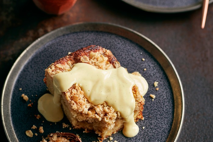 A dark blue plate topped with a slice of sponge pudding covered in custard